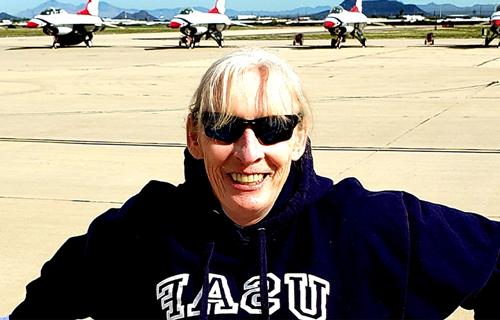 Annette Perkins stands smiling on a military base with jets in the background