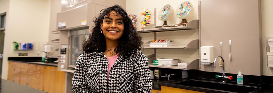 Briana Pomales stand smiling in a chemistry classroom