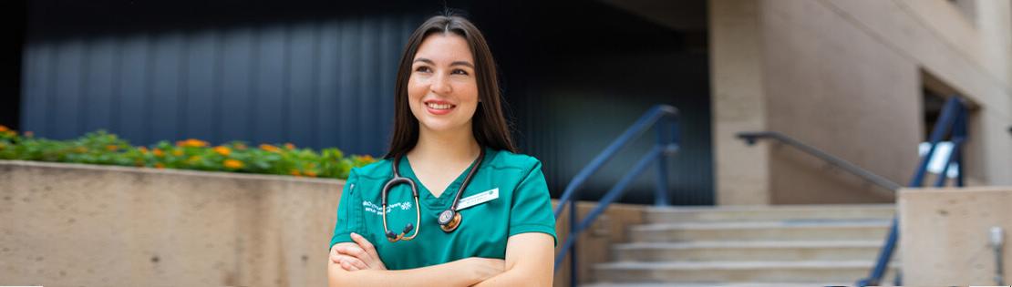 A medical assistant student smiles while wearing scrubs in a Pima West campus courtyard