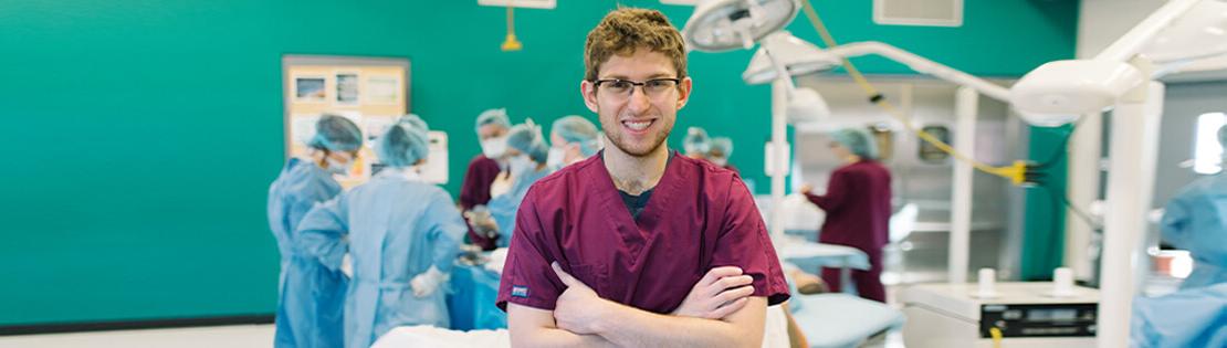 A surgical tech student poses for a photo while classmates practice behind him in a pima surgical class