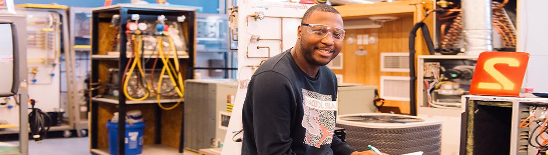 A student with safety glasses sits in a engineering class smiling