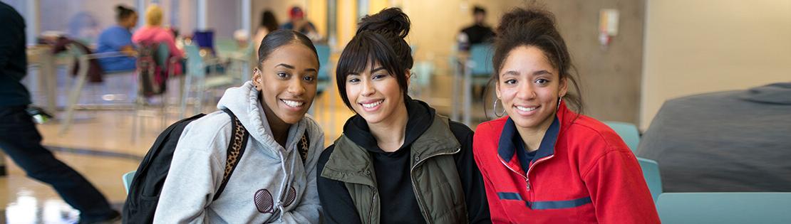 three students sit in a Pima Campus student lounge smiling 